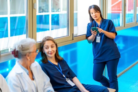 Asian nurse using a smartphone while colleagues chat and relax during a break in the hospital