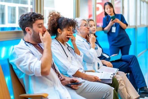 Exhausted medical professionals yawning while sitting on chairs in a hospital corridor,