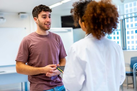 Young man holding a tablet, engaging in a conversation with a doctor inside a hospital room,