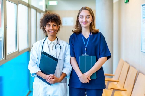 Doctor and nurse smiling while holding medical records in a hospital corridor, showcasing teamwork