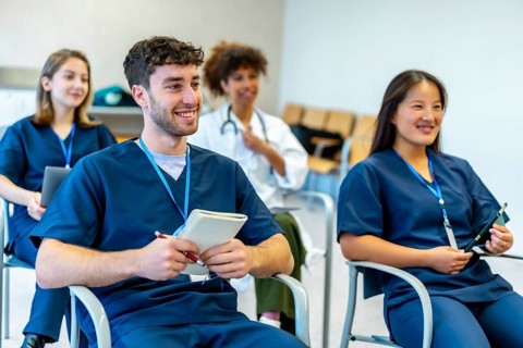 Group of smiling medical students attending a conference, taking notes and listening to the speaker