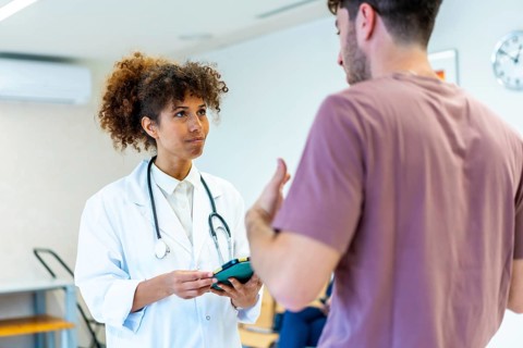 Doctor holding a tablet and listening to a patient explaining his symptoms in the waiting room of a
