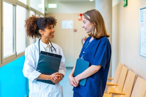 Female doctor and nurse engaging in a friendly conversation while reviewing medical records in a