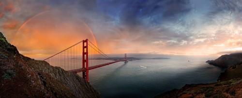 Panoramic view of the Golden Gate Bridge with a rainbow at sunset and orange-glowing storm clouds,