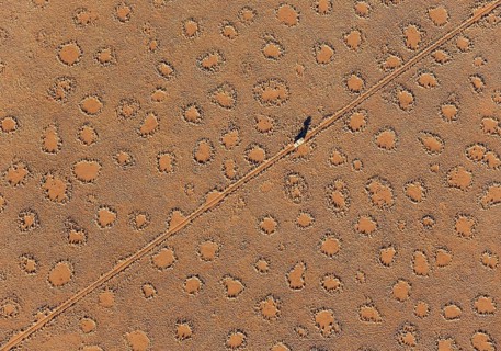 A vehicle of the balloon ground crew crosses a sandy plain with so-called Fairy Circles at the edge