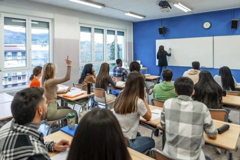 Multi ethnic university students listening to their teacher and raising their hand to answer a