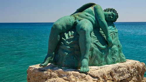Bronze sculpture, sleeping Eros, close-up of an artistic statue on a rock by the blue water,