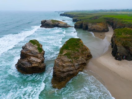 Gigantic, jagged rocks jutting out of the sea and lapped by foaming water, aerial view, Praia das