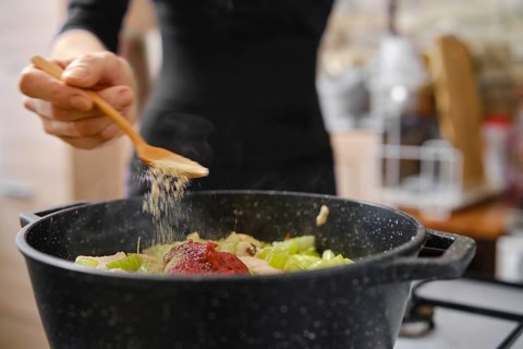Unrecognizable woman sprinkling spice over vegetables in a black pot while preparing a hearty meal