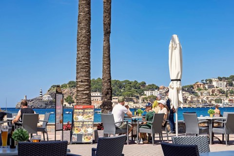 People sitting on a restaurant by the sea at a coast village at a tourist resort, Port de Sóller,