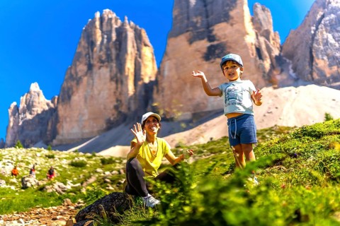 Mother and son waving while hiking on a sunny summer day near the tre cime di lavaredo, a symbol of