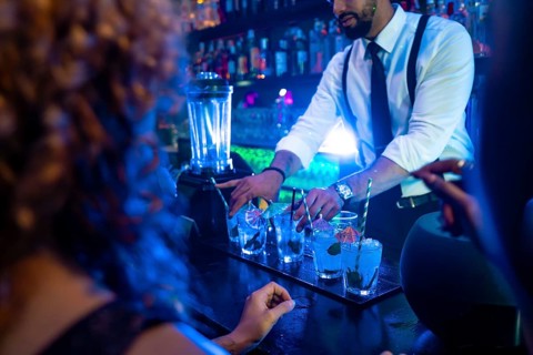 Professional bartender preparing cocktails at bar counter in nightclub, using fresh ingredients and