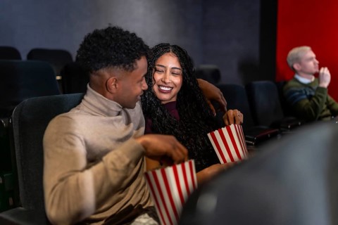 Happy couple enjoying a film in a cozy movie theater, sharing popcorn and laughing together,