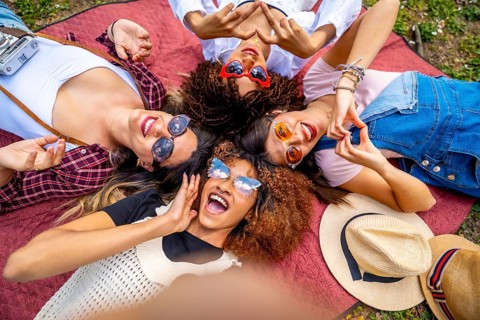 Four multi ethnic female friends are lying in circle on blanket in a park, making heart shape with