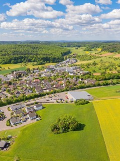 Aerial view of a village surrounded by fields and forests under a slightly cloudy sky, Gechingen,