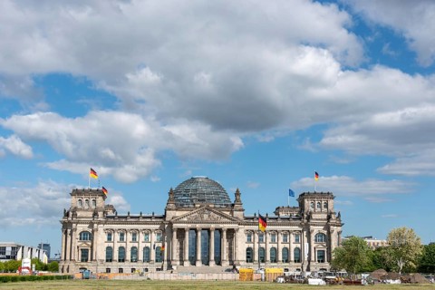 Front view of the Reichstag under a cloudy sky with waving flags, Berlin, Germany