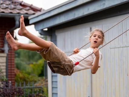 Boy swinging while sitting on children's swing at shed and garden gate, Germany