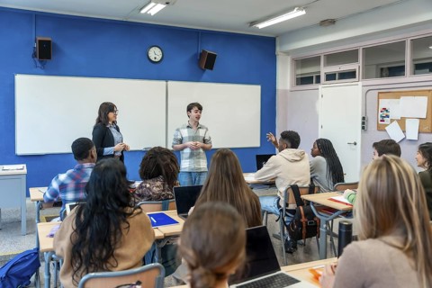 Male high school student giving a presentation in front of his diverse classmates and teacher in a