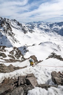 Mountaineer climbing up a steep snow slope, secured by a rope, ascent to the summit of Piz