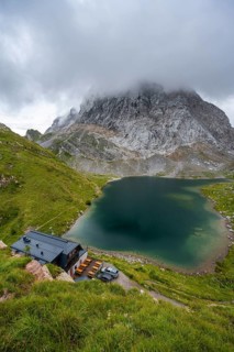 Alpenverinshütte Wolayerseehütte on Lake Wolayersee, cloudy mountain landscape with green meadows