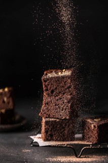 Composition of little stack of tasty sweet brownie cuts with powder on black background
