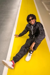 Vertical photo of an african modern musician sitting on the ground in an urban space
