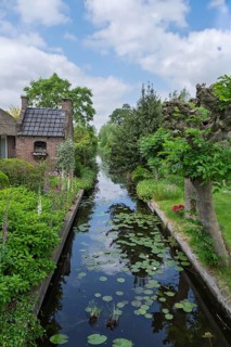 Idyllic landscape with a canal between gardens and a brick house, surrounded by green vegetation