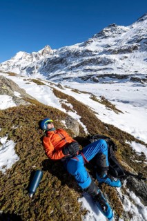 Ski tourer taking a break in the sun, lying down, taking a nap, snowy mountain landscape in winter,