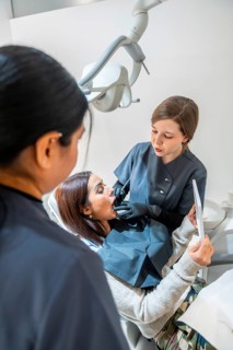 Dentist examining patient's teeth with dental tools while a nurse assists in a bright, modern