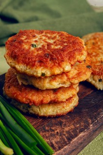 Crispy potato pancakes Latkes, stacked on a wooden board next to fresh green onions, natural light,