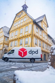 A DPD delivery van stands in front of a yellow-painted half-timbered building covered in snow,