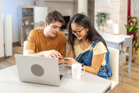 Young multiethnic couple using a credit card and a laptop to make an online purchase from their