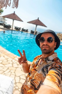Tourist man in the hotel pool in summer taking a selfie enjoying the vacation, making the victory