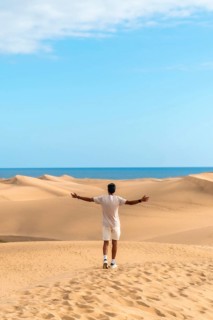 Young man opening arms in maspalomas dunes, gran canaria, feeling freedom and enjoying the desert