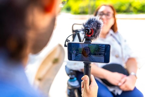 Videographer holding a smartphone on a tripod with external microphone, recording an interview with