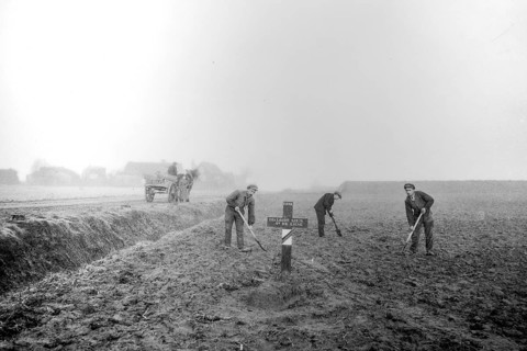 Wooden cross on grave of fallen soldier and workers levelling field on former battlefield after the