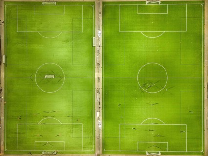 Two symmetrical football pitches from a bird's eye view with scattered players on the green pitch