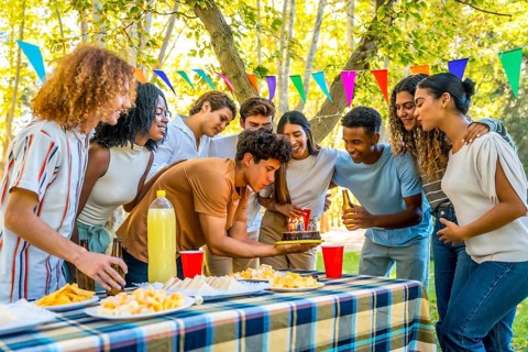 Young man celebrating birthday during picnic with multi-ethnic friends in a park