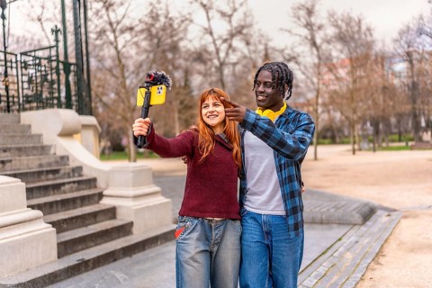 Two young content creators are recording a video for their vlog using a smartphone with a