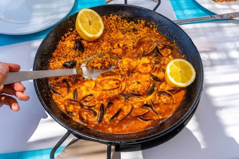 Close up of a spoon scooping up seafood paella from a traditional paella pan, garnished with lemon