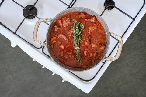 A pot of beef stew is bubbling on a white stove, filled with tender meat, colorful vegetables, and