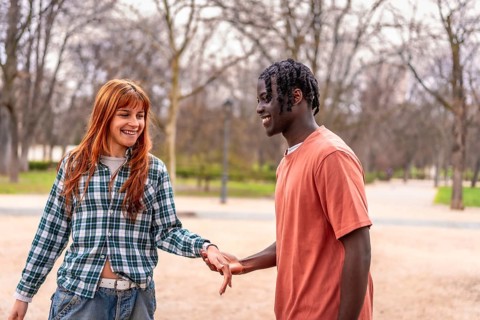 Young interracial couple holding hands and smiling while walking in a park, enjoying a romantic