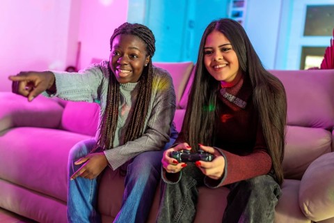 Two friends enjoying their free time playing video games at home, sitting on a comfortable sofa in