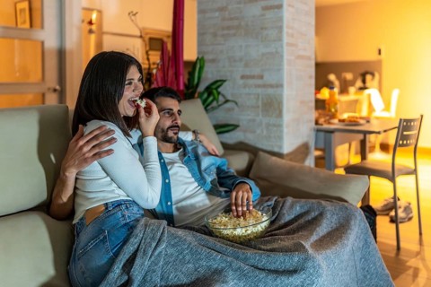 Young couple enjoying a movie night at home, eating popcorn from a bowl and relaxing on the sofa
