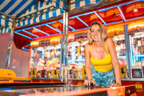 Blonde caucasian smiling woman playing arcade games at night in an amusement park