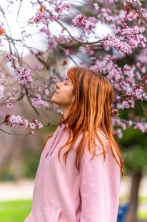 Young woman with long red hair, wearing pink hooded sweatshirt, breathing fresh air and enjoying