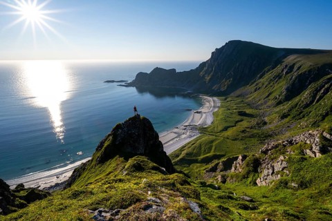 Climber on a rock, view of picturesque coastal landscape with sun star, steep coast with peak