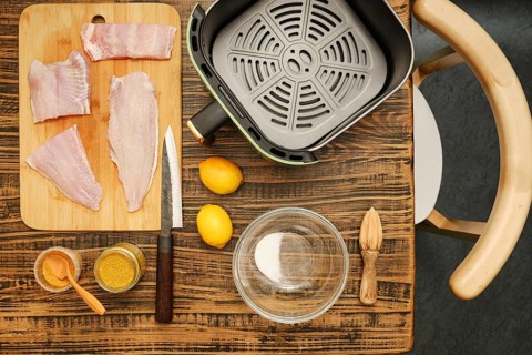 Fish fillets are arranged on a cutting board next to a bowl and spices. Fresh lemons rest nearby,