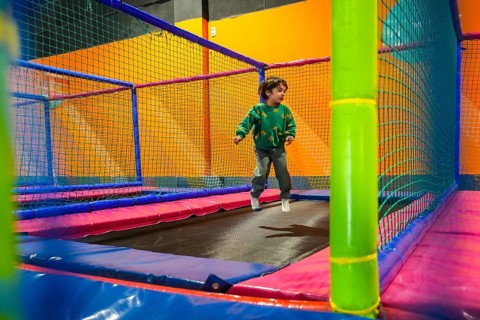 Young boy enjoying playtime, bouncing on a trampoline inside a vibrant and safe indoor play area