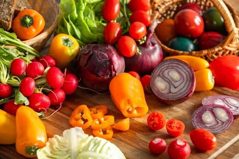 Mix of fresh vegetables such as peppers, onions and tomatoes, on a wooden board next to Easter eggs
